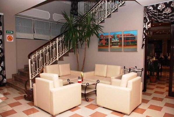 Um hall de hotel com uma escadaria, área de estar com dois sofás, mesa de centro e um vaso de planta.