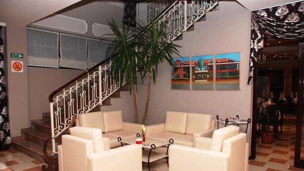 A hotel lobby with a staircase, a seating area with two sofas, a coffee table, and a potted plant. - Univers (Elbasan)