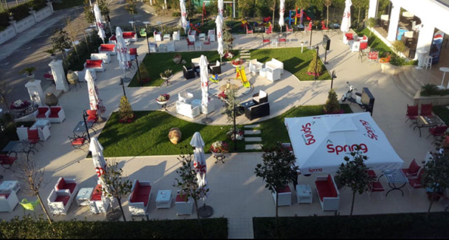 Un espace extérieur aménagé avec des tables blanches et des coussins rouges, entouré de parasols blancs et de plantes en pot.