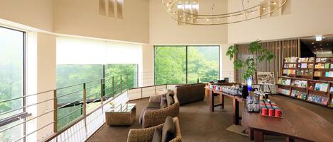A spacious room with a balcony, wicker furniture, a wooden table with red cups, and a bookshelf with books.