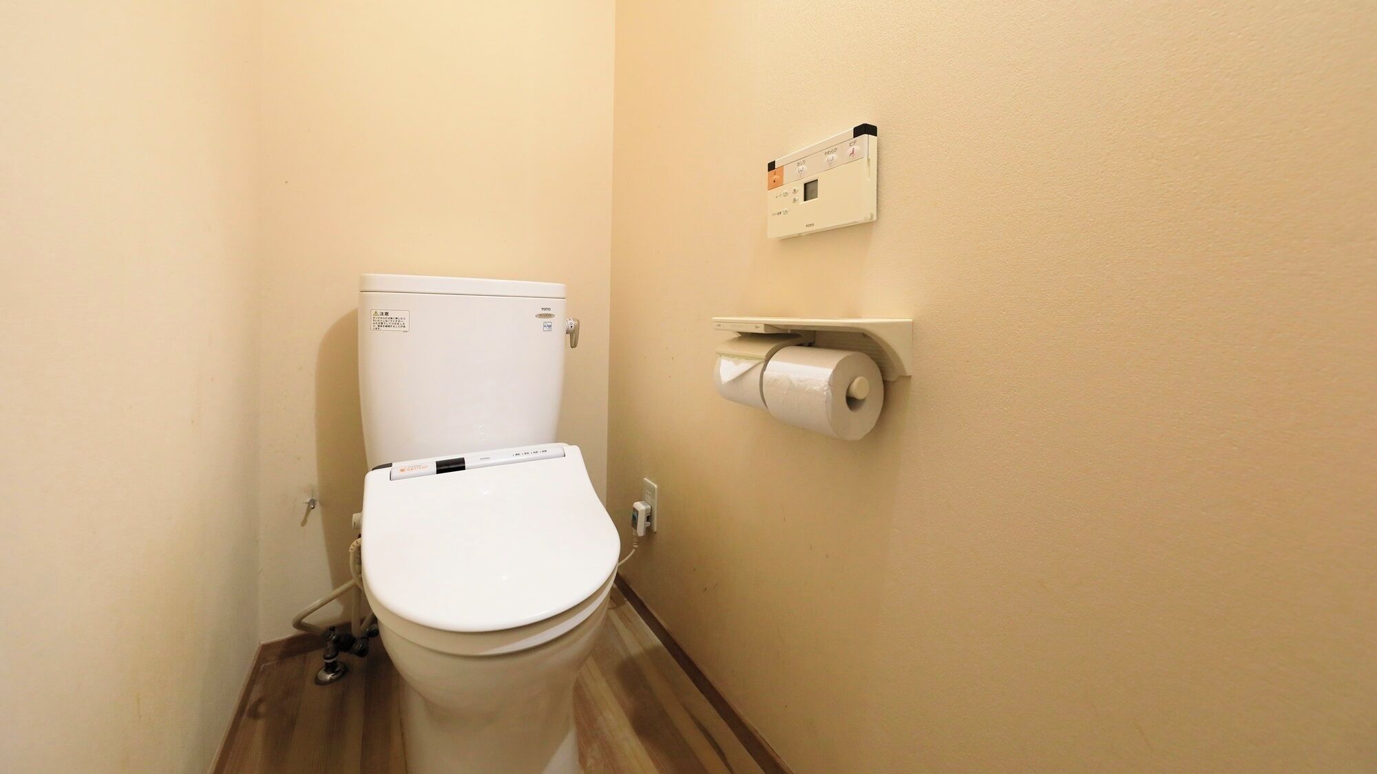 A small bathroom with a toilet, a toilet paper holder, and a wall-mounted control panel.