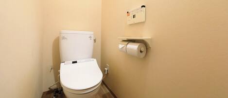 A small bathroom with a toilet, a toilet paper holder, and a wall-mounted control panel.