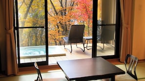 A room with a large sliding glass door leading to a deck with outdoor seating and a view of autumn foliage. - Okunikko Hotel Shikisai (Nikko)