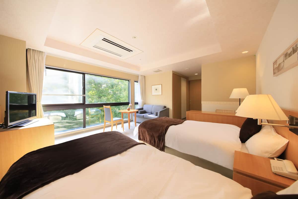 Habitación de hotel con dos camas, televisión, escritorio, lámpara y vistas a zonas verdes.