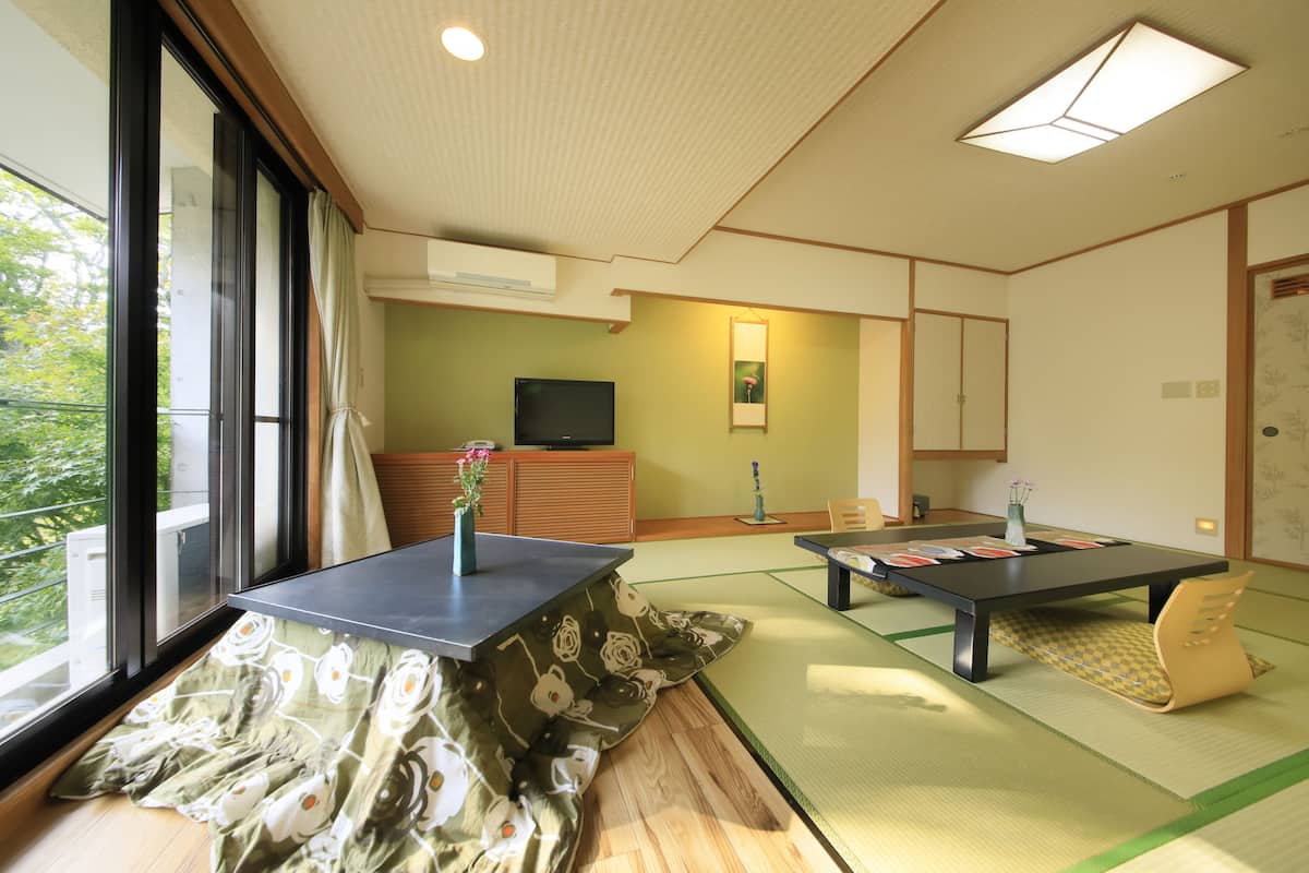 Una habitación tradicional japonesa con suelo de tatami, una mesa baja y un televisor sobre un mueble de madera.