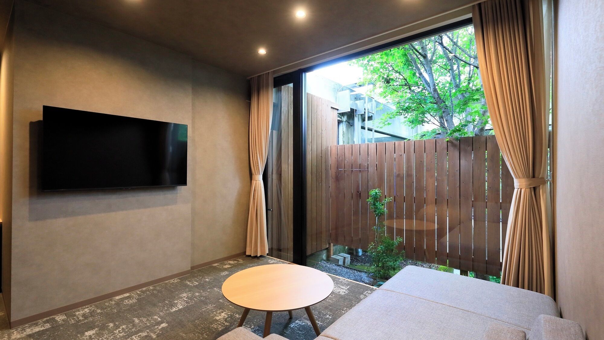 A room with a flat-screen TV mounted on the wall, a round table, and a sofa.