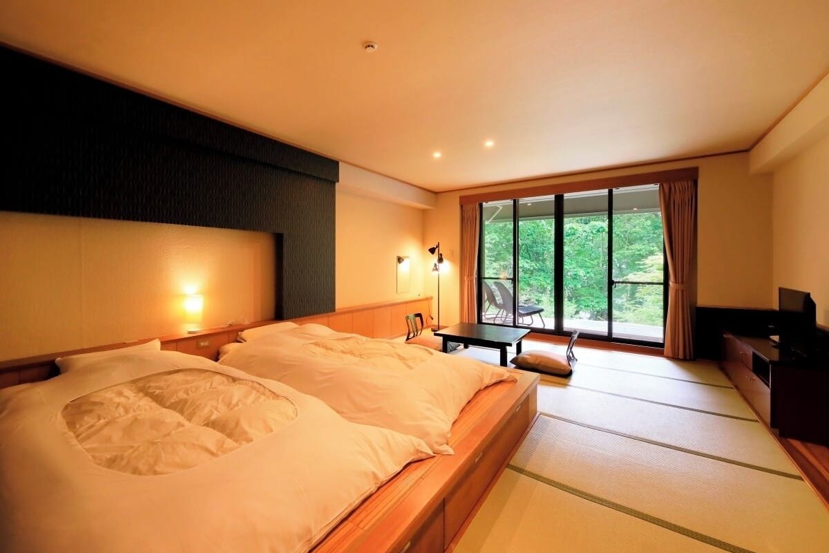 Habitación de hotel con una cama grande, un escritorio y vista a zonas verdes por la ventana.