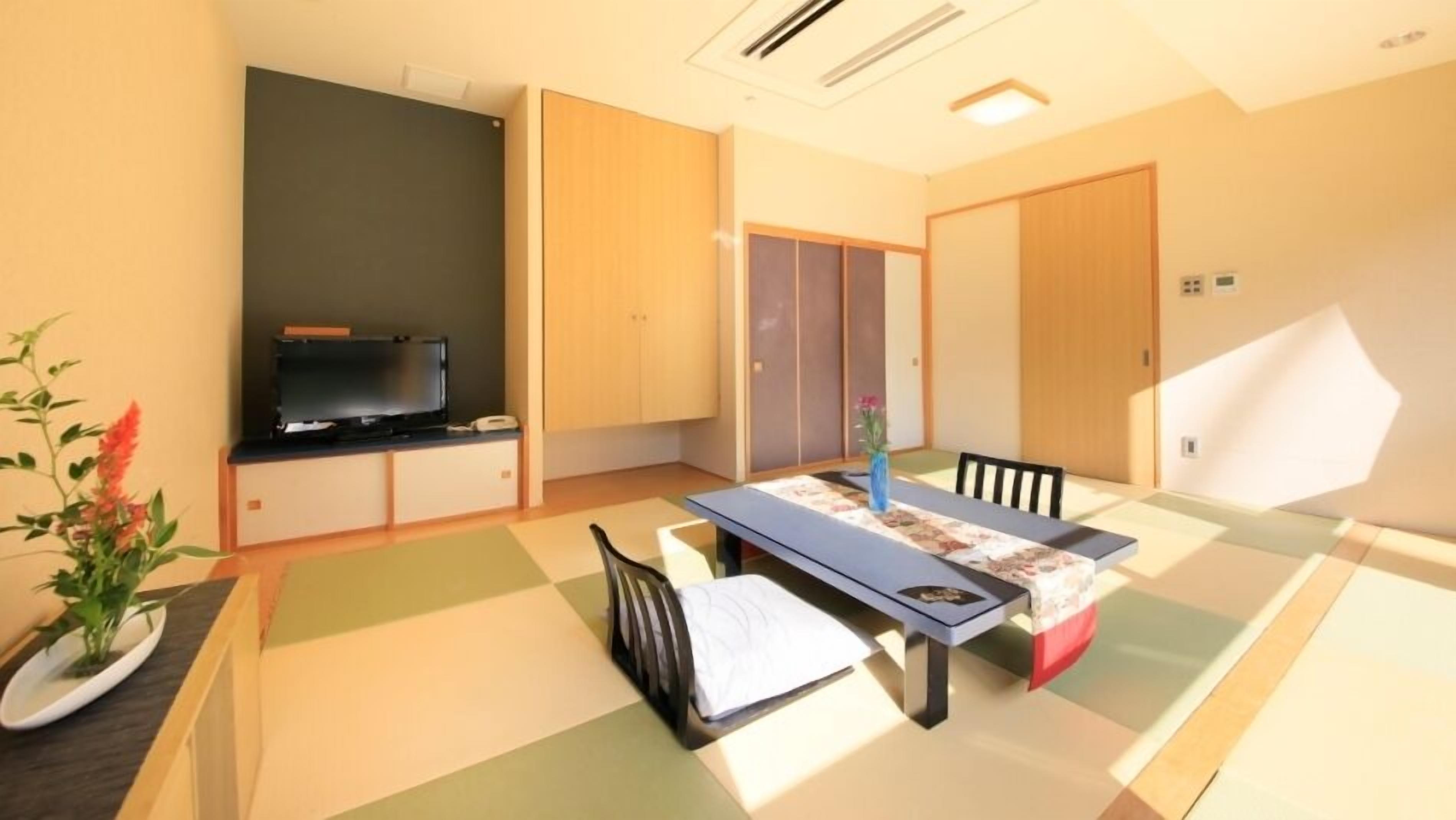 Ein Zimmer mit Fernseher, einem Esstisch mit Stühlen, einer kleinen Pflanze und Schiebetüren.
