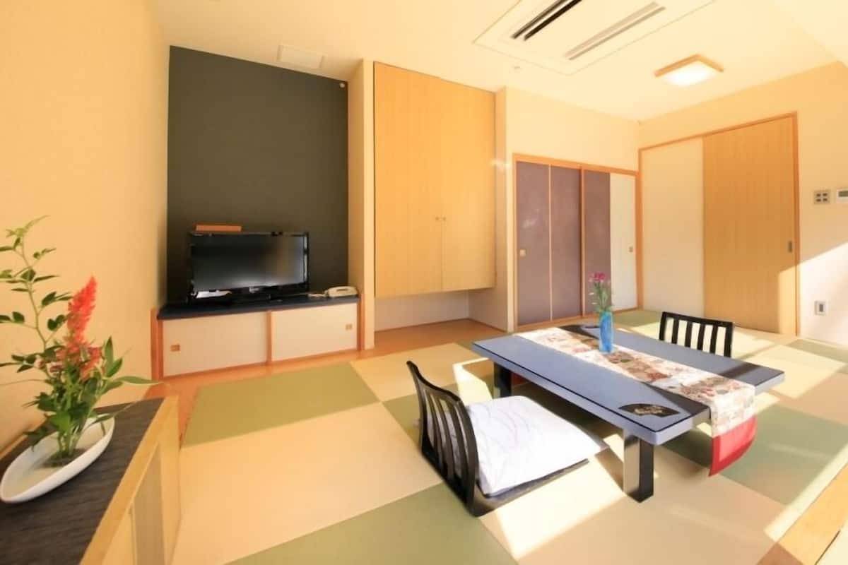 Una habitación con televisión, una mesa de comedor con sillas, una planta pequeña y puertas correderas.