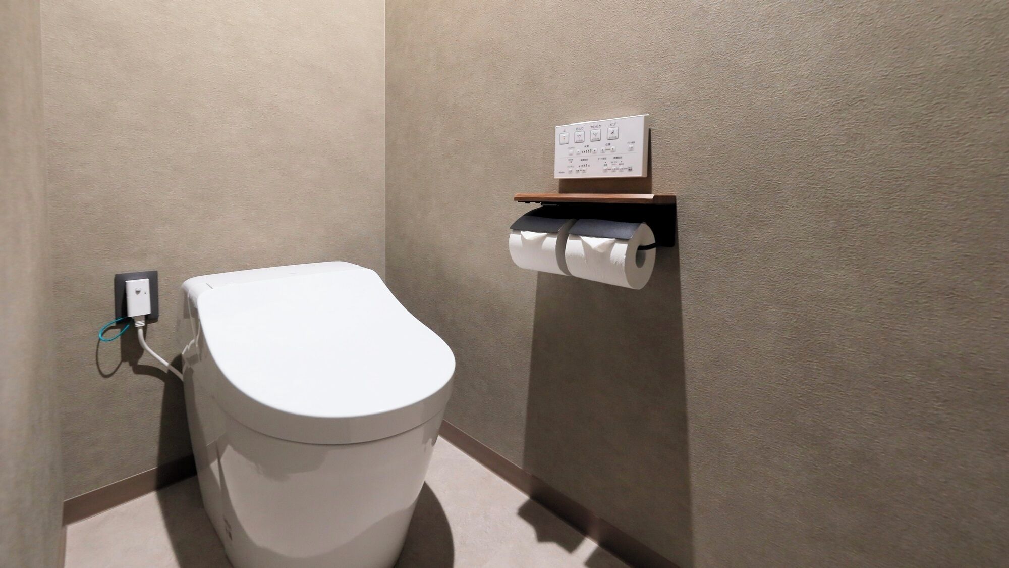 A modern bathroom with a white toilet, a wall-mounted paper towel holder, and a power outlet.