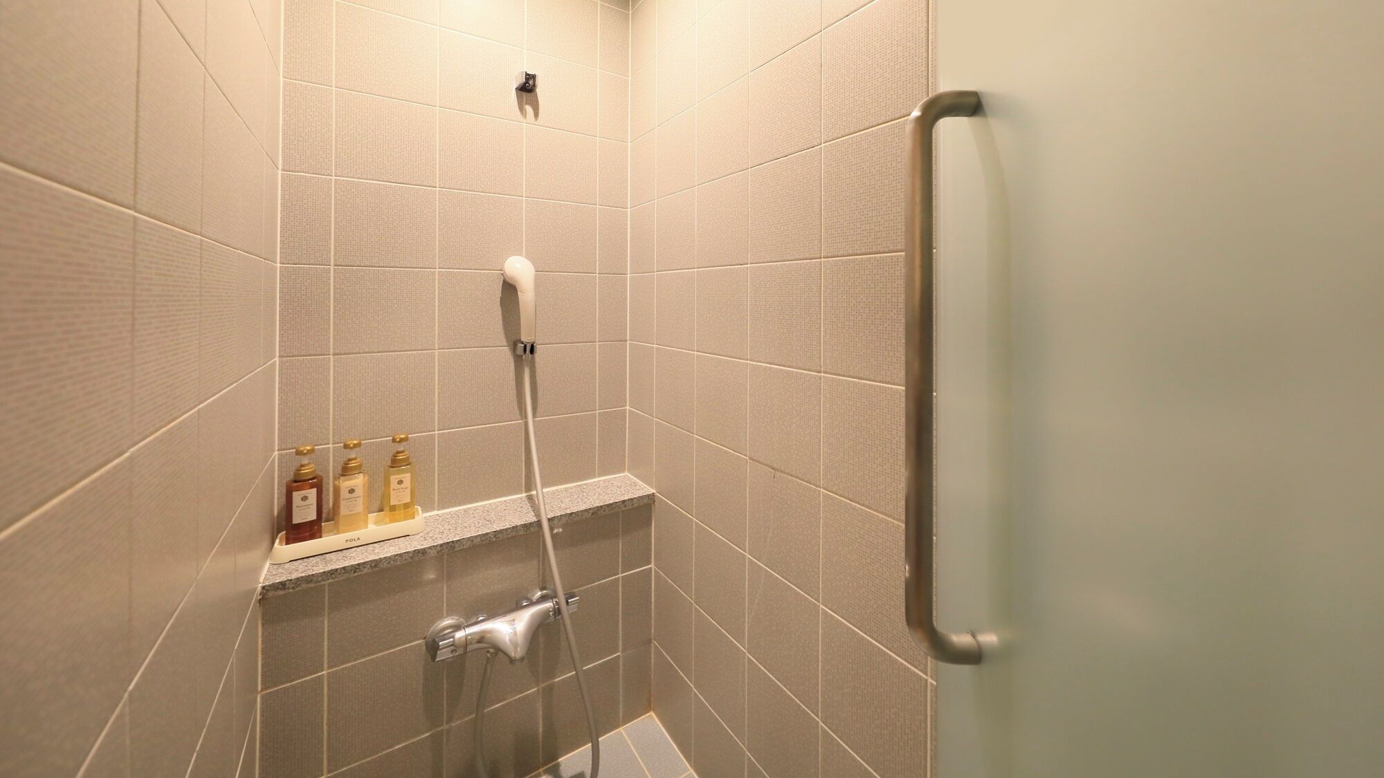 A shower area with a handheld showerhead, a wall-mounted faucet, and a shelf with toiletries.