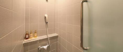 A shower area with a handheld showerhead, a wall-mounted faucet, and a shelf with toiletries.
