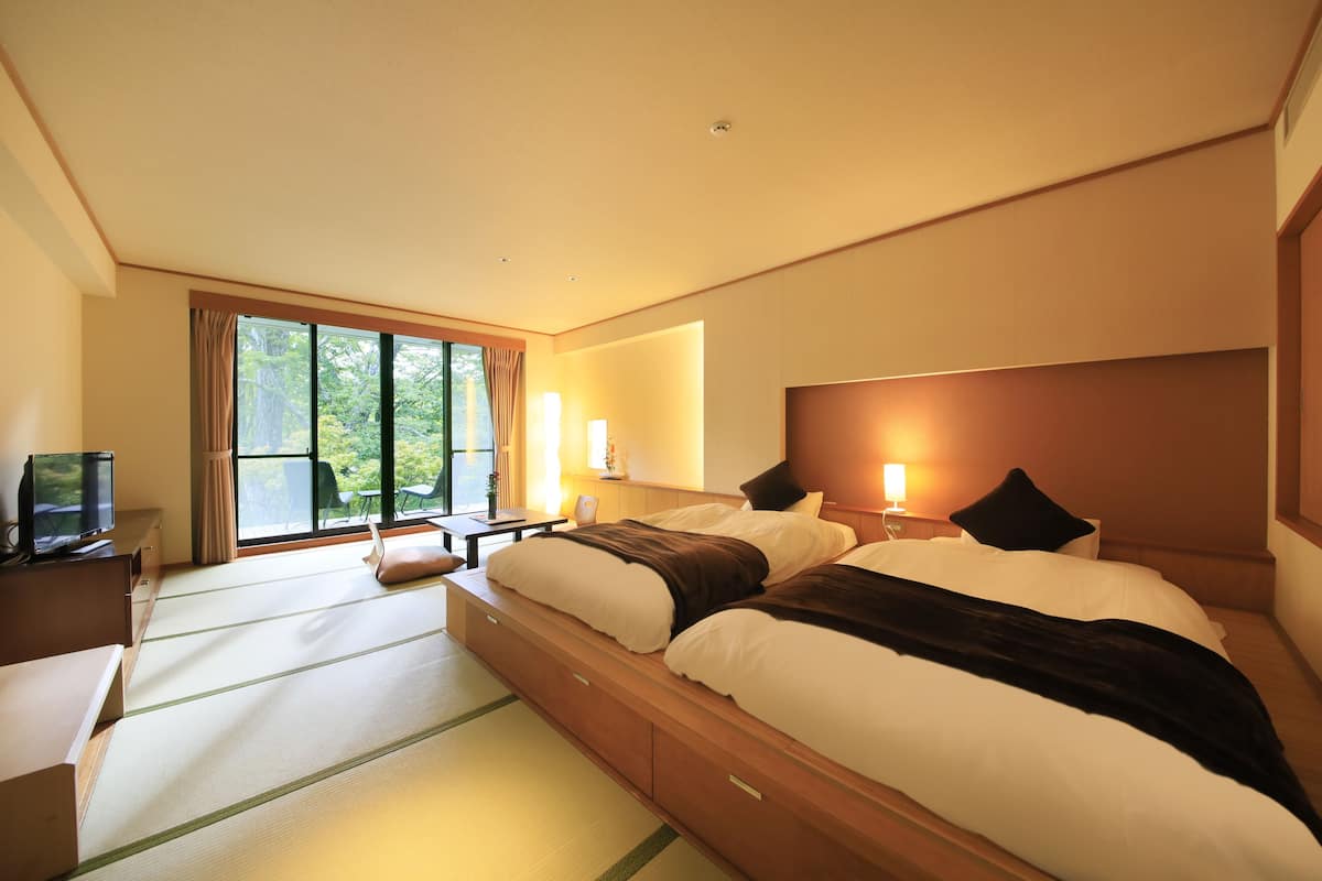 Habitación de hotel con una cama grande, un escritorio y un televisor. Cuenta con una ventana con cortinas y vistas al exterior con vegetación.