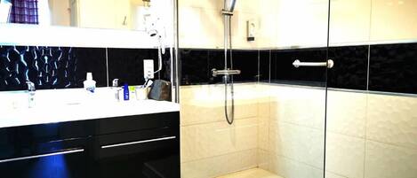 A modern bathroom with a glass shower enclosure, a white sink with a black countertop, and a mirror above the sink.