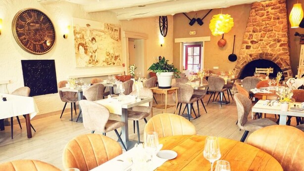 Een restaurant met ronde tafels, gestoffeerde stoelen, een stenen openhaard en een grote klok aan de muur.