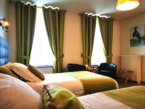 Une chambre d’hôtel avec deux lits, un bureau, des chaises et un radiateur.