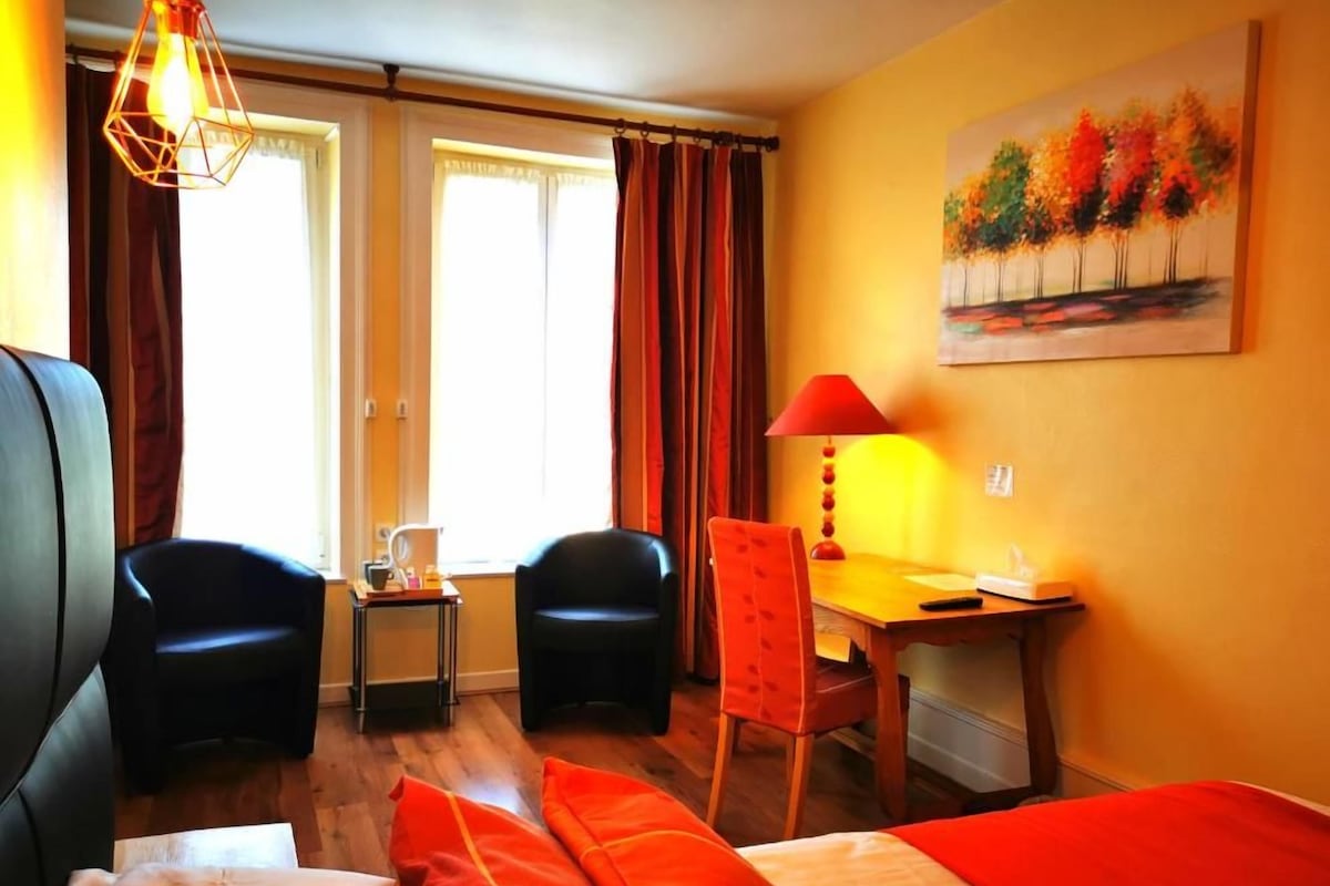 Une chambre d’hôtel avec un lit, deux chaises, un bureau et un tableau au mur.