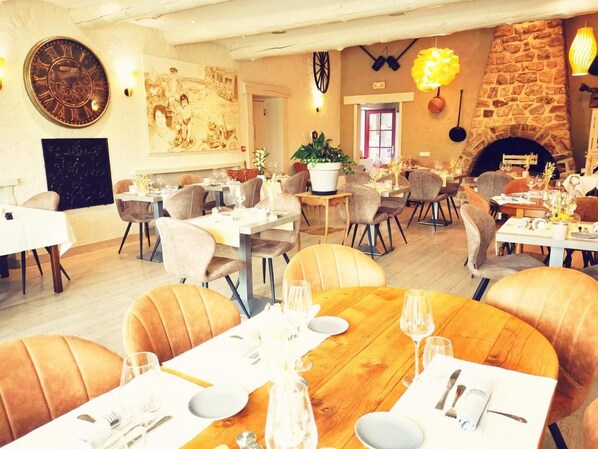A restaurant with round tables, chairs, and a stone fireplace.