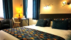 Een hotelkamer met een bed, een bureau met stoel, een lamp en een wandlamp.