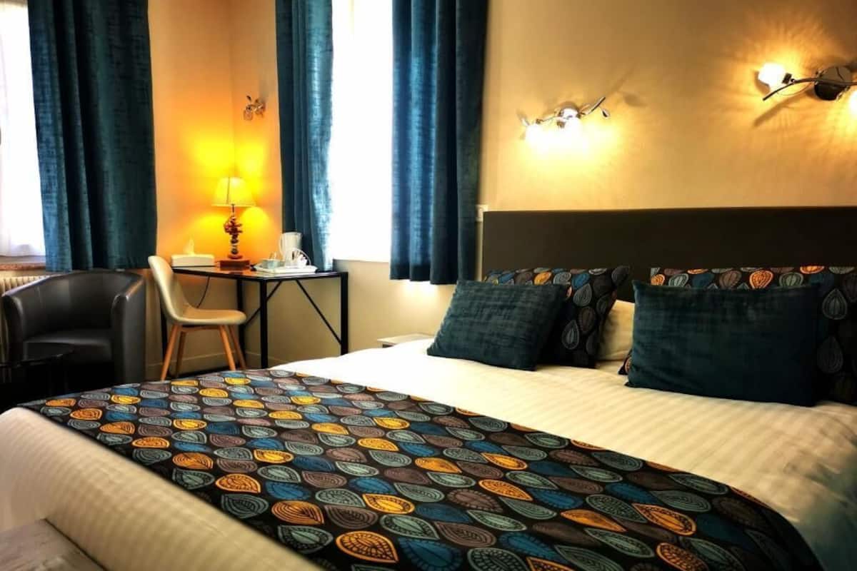 Een hotelkamer met een bed, een bureau met stoel, een lamp en een wandlamp.