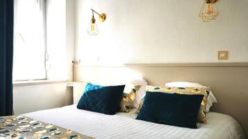 A hotel room with a bed, two wall-mounted lamps, a window with curtains, and a bedside table.