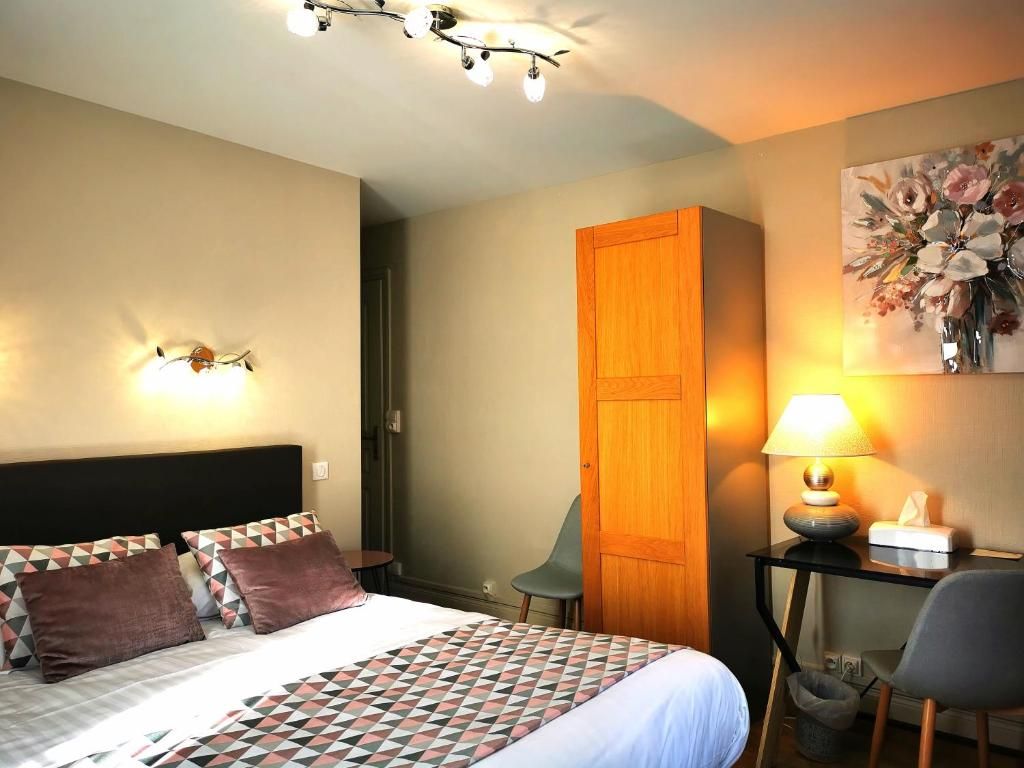 Una habitación de hotel con cama, escritorio, silla, armario y un cuadro en la pared.