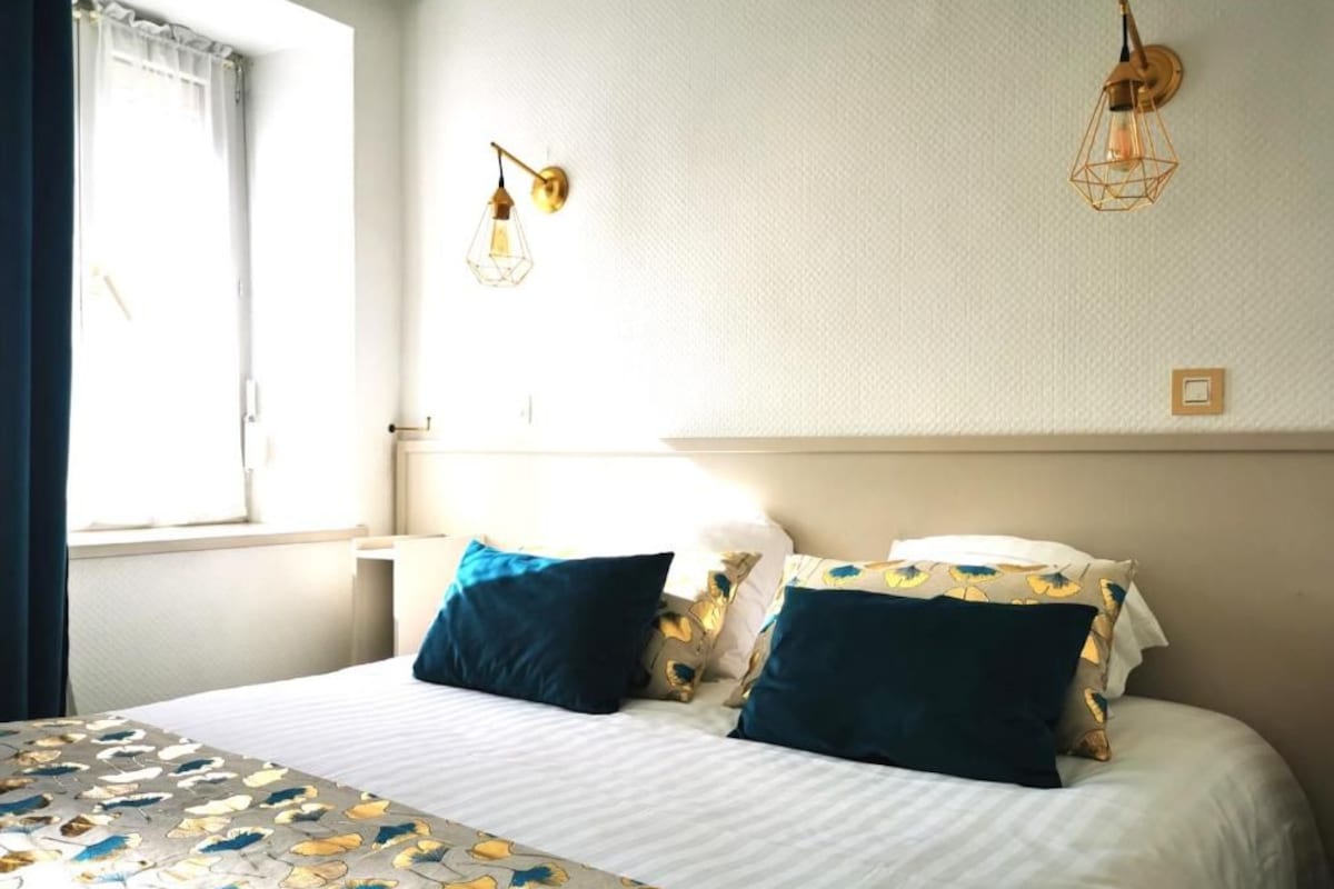 Une chambre d’hôtel avec un lit, deux lampes fixées au mur, une fenêtre avec des rideaux et une table de chevet.