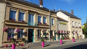 A two-story building with a ground-floor entrance, a balcony with hanging flower baskets, and a sign indicating a restaurant. - Hotel La Sapiniere (Remilly-Aillicourt)