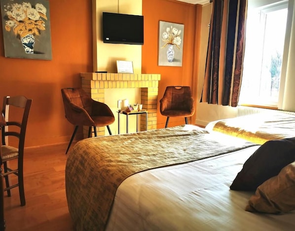 Una habitación de hotel con una cama, dos sillones, una chimenea y obras de arte en las paredes.