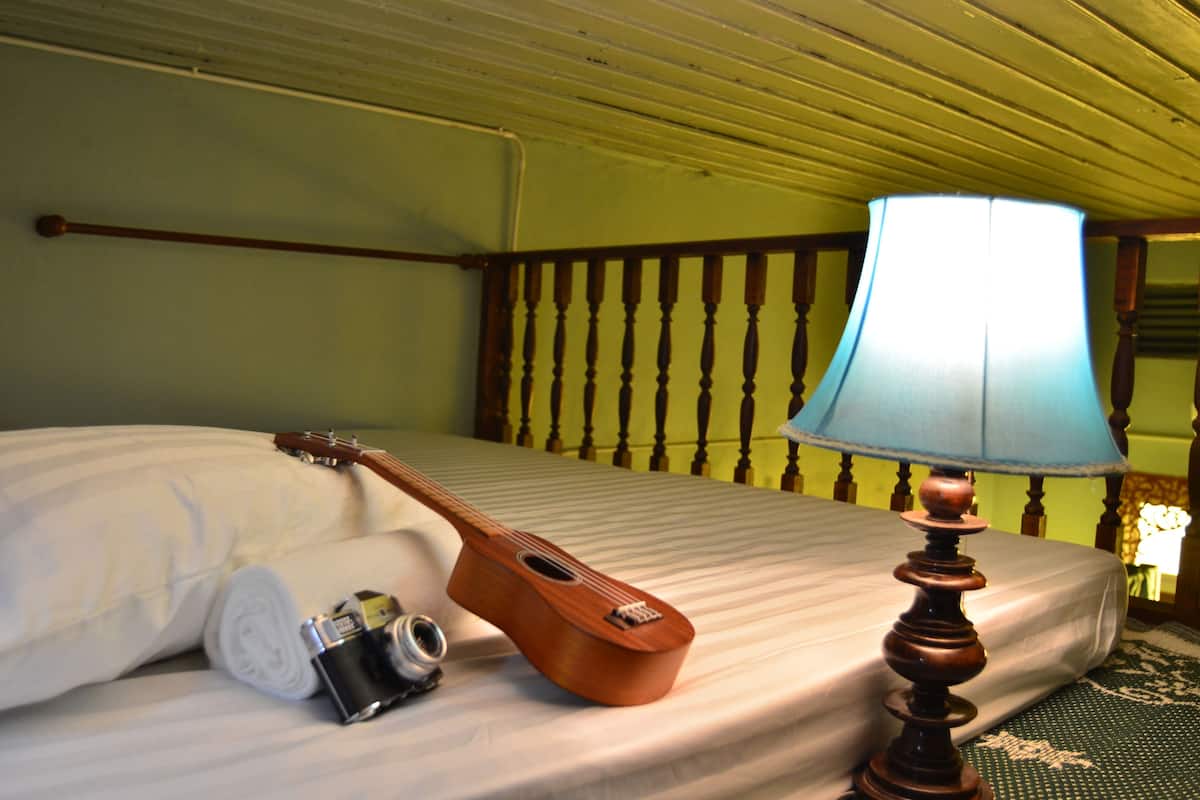 A bed with a wooden guitar, a camera, and a lamp.