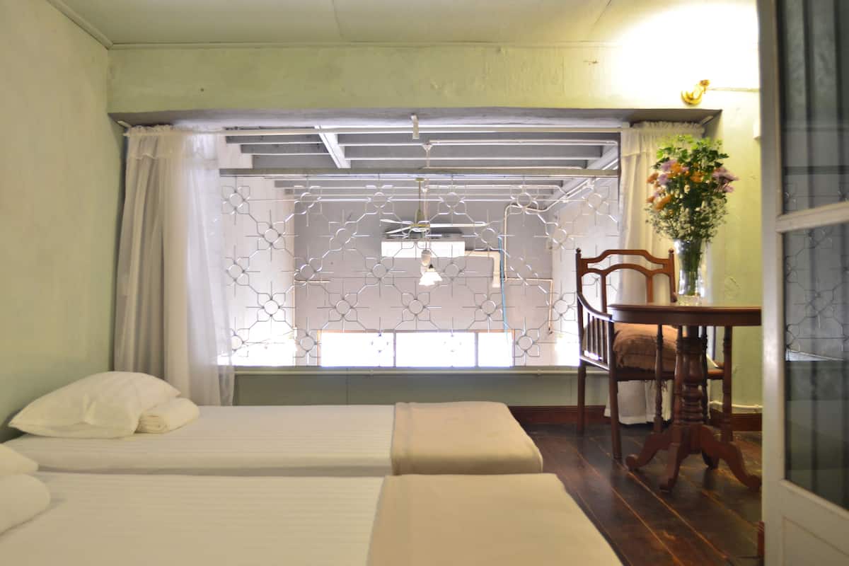 A hotel room with two beds, a wooden chair, a table, and a window with a decorative screen.