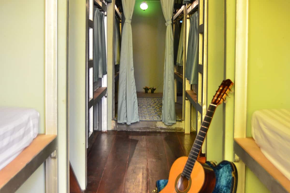 A narrow hallway with bunk beds on either side, a guitar leaning against a wall, and a ceiling fan.