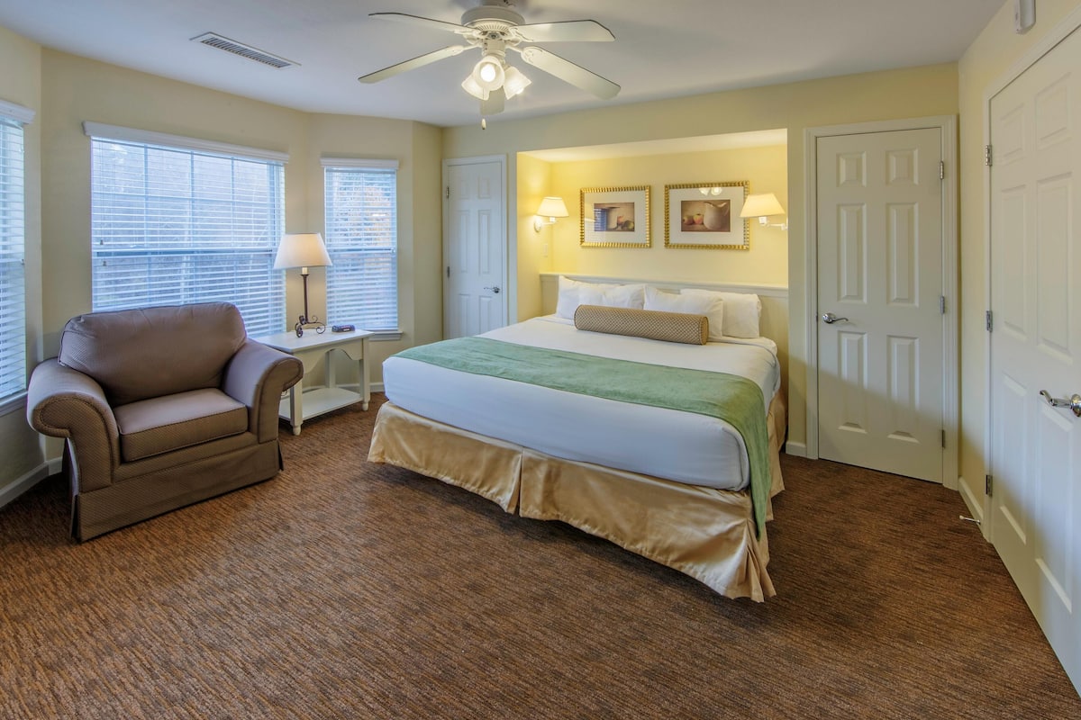 Ein Schlafzimmer mit Bett, Sessel, Schreibtisch und Deckenventilator.