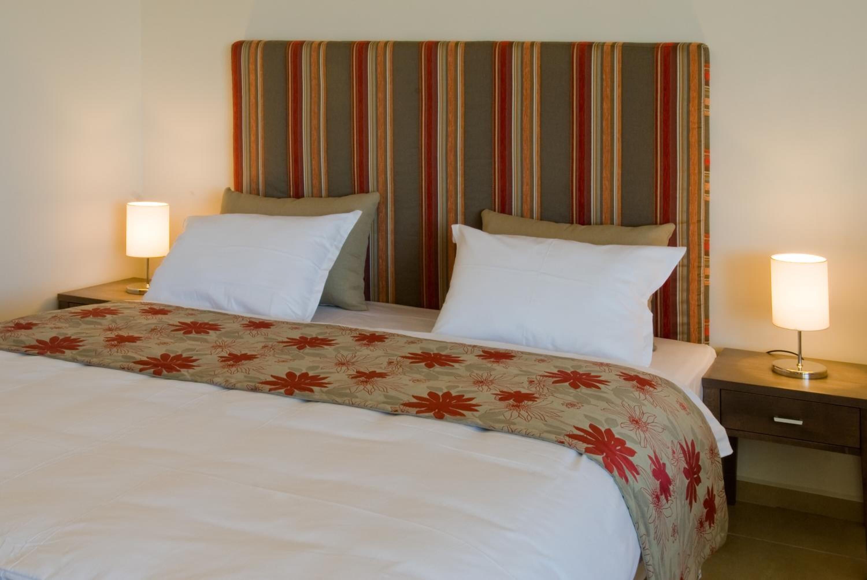 A double bed with a floral-patterned bedspread, two bedside lamps, and a striped headboard.