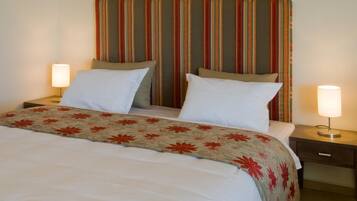 A double bed with a floral-patterned bedspread, two bedside lamps, and a striped headboard.