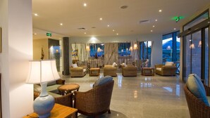 A spacious lobby with wicker furniture, a polished floor, and large windows offering a view of a mountain. - South Pearl Apart Complex (Sozopol)
