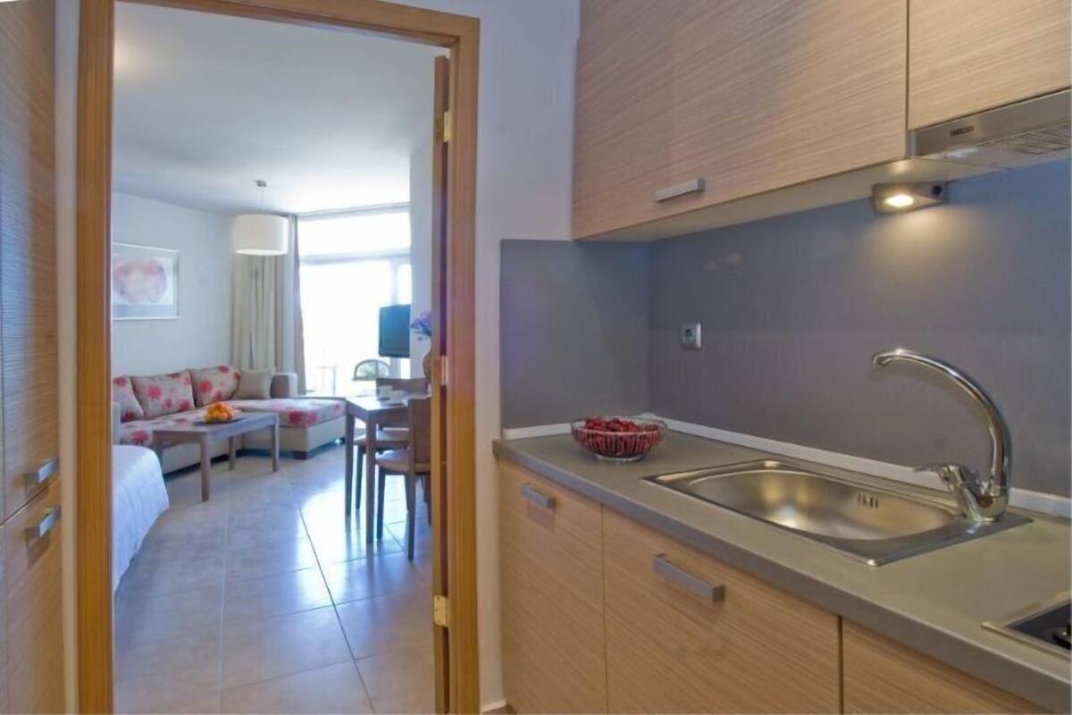A modern kitchen with a stainless steel sink, wooden cabinets, and a bowl of fruit on the counter.
