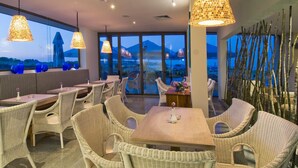 A restaurant with wicker furniture and large windows offering a view of mountains. - South Pearl Apart Complex (Sozopol)