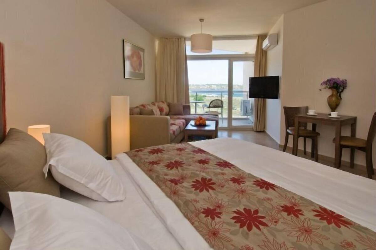 A hotel room with a bed, a sofa, a TV, a desk, and a balcony with a view.