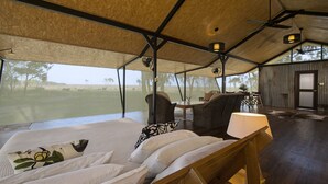 A spacious room with a large bed, wicker chairs, and a view of a grassy field.