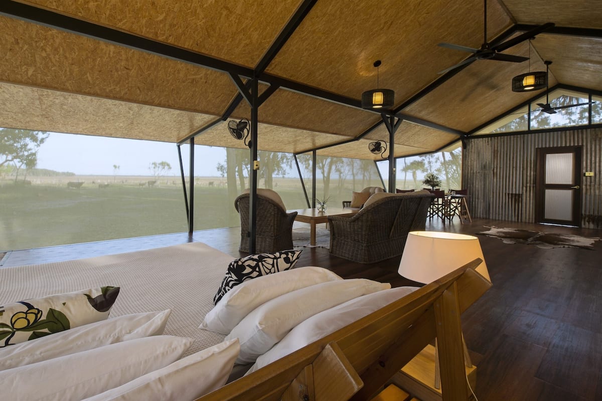 A spacious room with a large bed, wicker chairs, and a view of a grassy field.