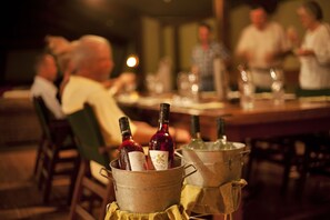 A dining area with tables and chairs, bottles of wine in a bucket, and a candle on the table.