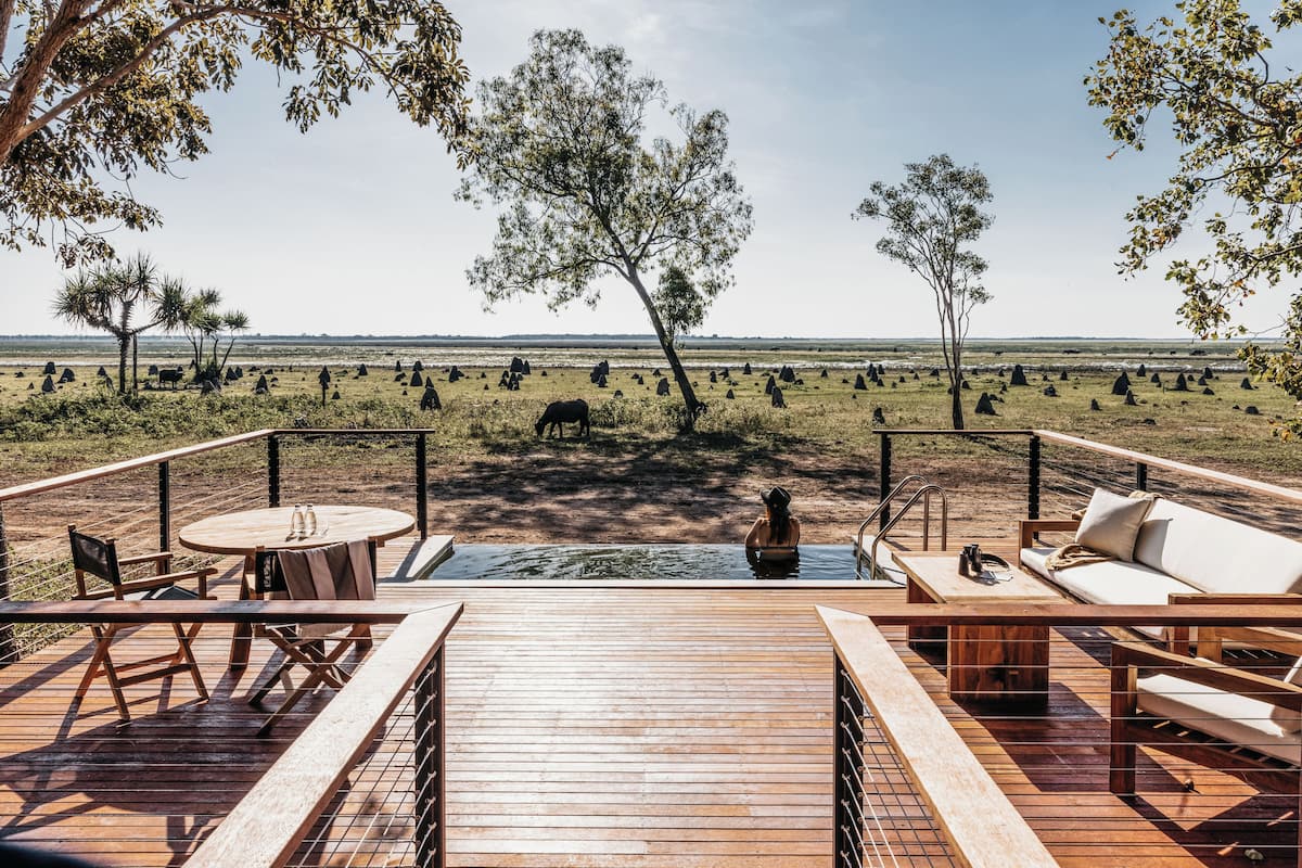 A wooden deck with outdoor seating, a pool, and a view of a savanna landscape with trees and wildlife.