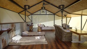 A spacious tented accommodation with a high ceiling, wooden flooring, and a central seating area with a sofa and chairs.