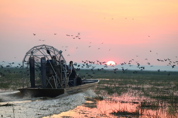 A boat with a cage structure on a body of water during sunset.