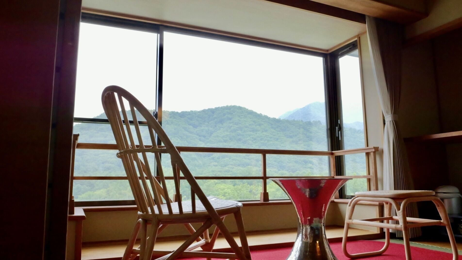 A room with a large window, a wooden chair, a small table, and a red floor mat.