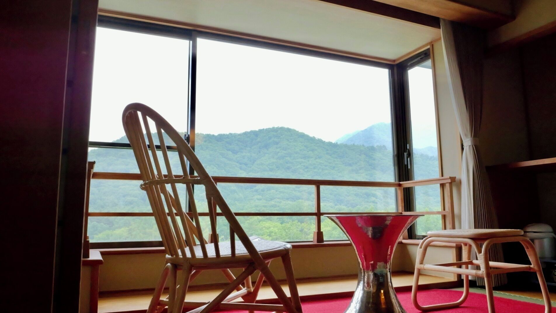 A room with a large window, a wooden chair, a small table, and a vase.