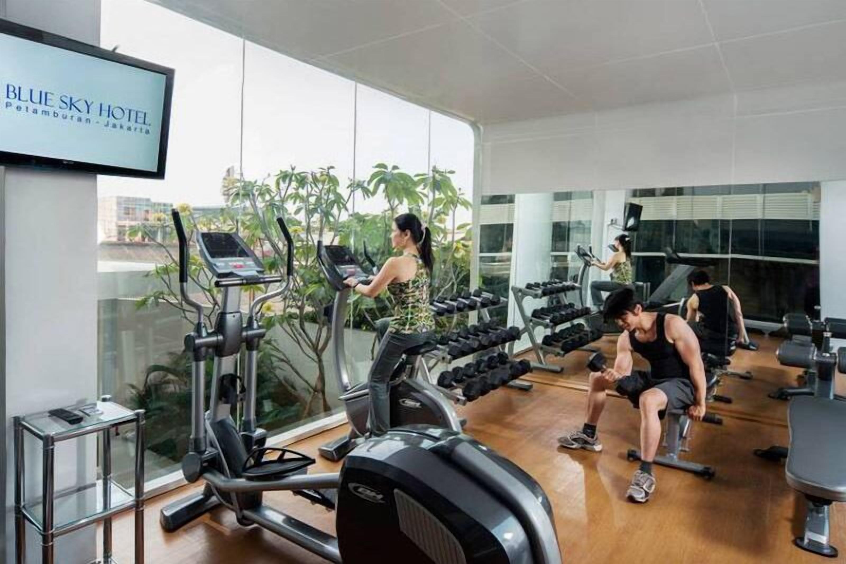 A gym with treadmills, dumbbells, and a TV displaying 'BLUE SKY HOTEL'.