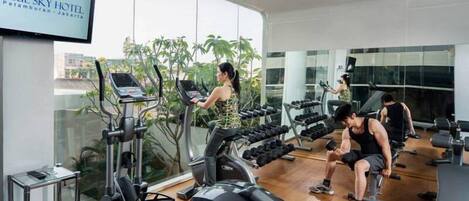A gym with treadmills, dumbbells, and a TV displaying 'BLUE SKY HOTEL'.