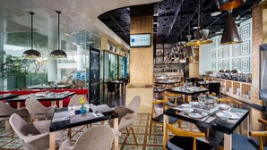 Um restaurante moderno com mesas pretas e de madeira, cadeiras cinzas e um chão estampado.